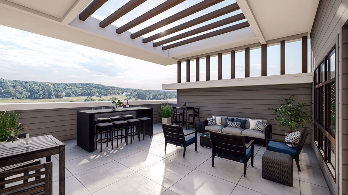 Outdoor patio area with modern furniture including a bar with stools, a seating area with a sofa and chairs, and a small table with chairs. The space has a partial pergola overhead and overlooks a scenic view of trees and hills in the distance.