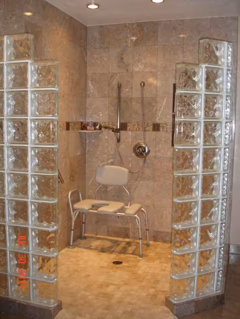 Accessible shower with a folding chair, grab bars, and tiled walls.