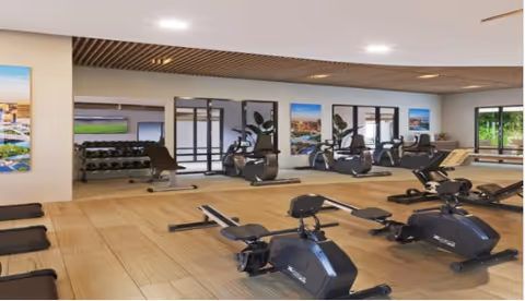 Bright fitness room with exercise bikes, rowing machines, mats, and a weight rack reflected in wall mirrors.