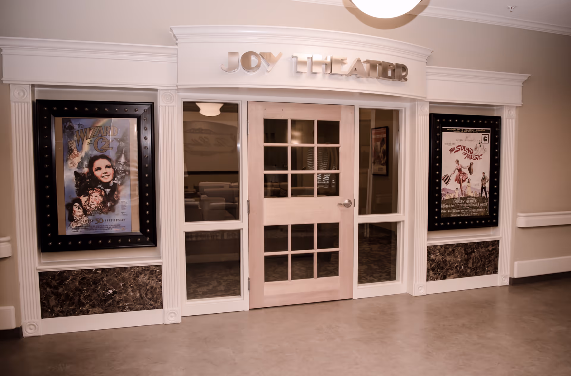 Entrance to the Joy Theater with glass-paned double doors flanked by framed movie posters for The Wizard of Oz and The Sound of Music.