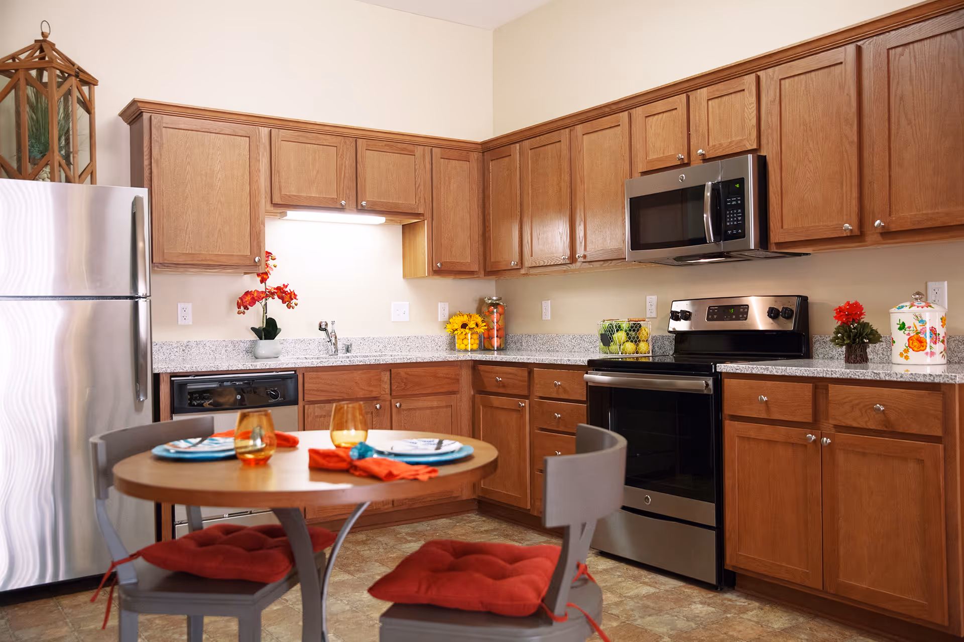 Bright kitchen with wooden cabinets, stainless steel refrigerator and stove, and a small round dining table set for two.