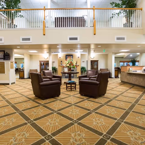 A spacious lobby lounge with four leather armchairs arranged around a small table on a patterned carpet beneath an open second-floor railing.