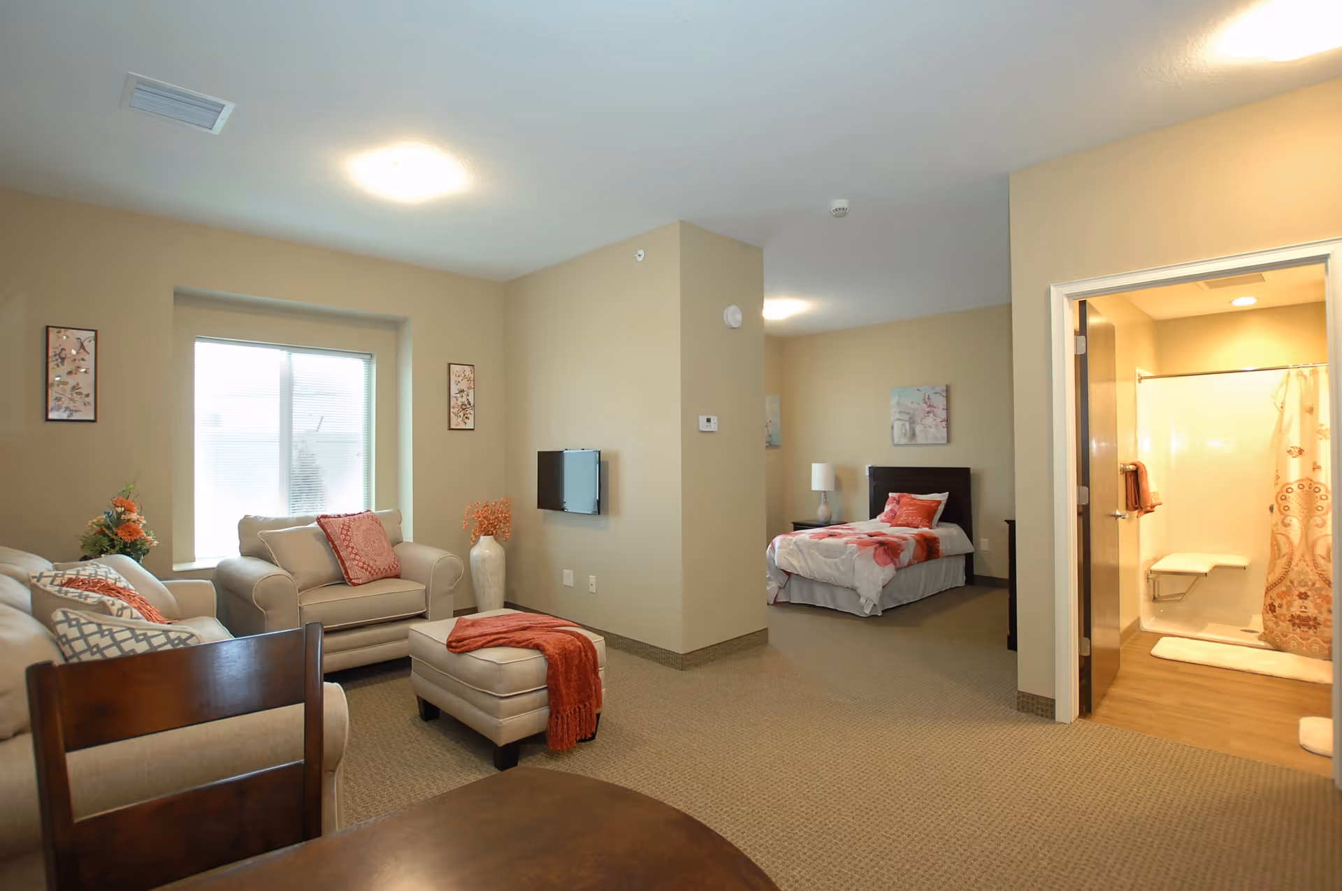 Open-plan senior suite with a seating area (sofa and ottoman), a bed in an alcove, and an adjacent bathroom visible.