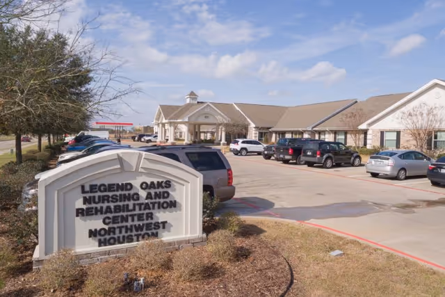 Front exterior view of Legend Oaks Nursing and Rehabilitation Center - Northwest Houston with the facility sign, entrance canopy, and parked cars in the driveway.
