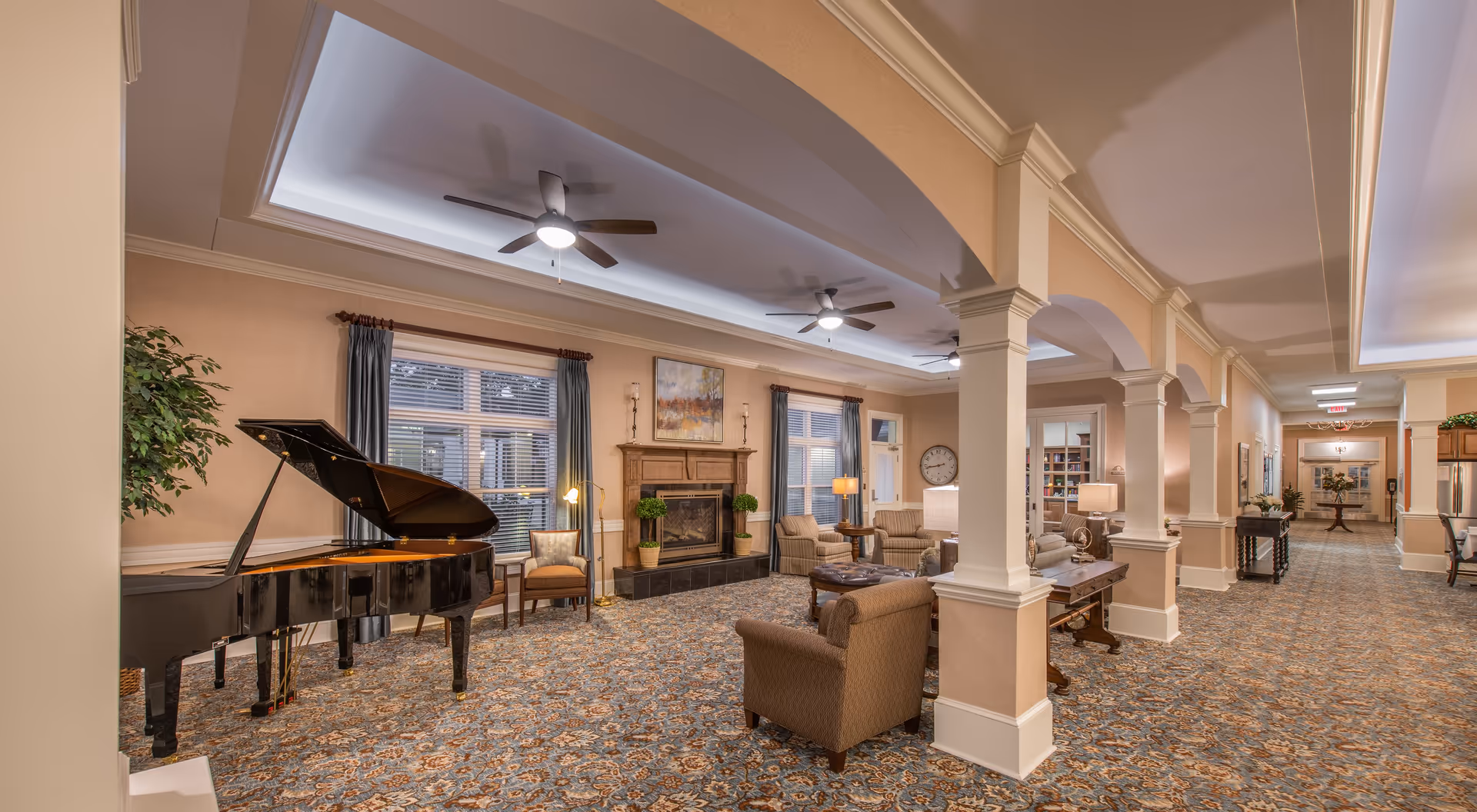 Spacious, elegant common living room with a grand piano, seating area, fireplace, and decorative columns.