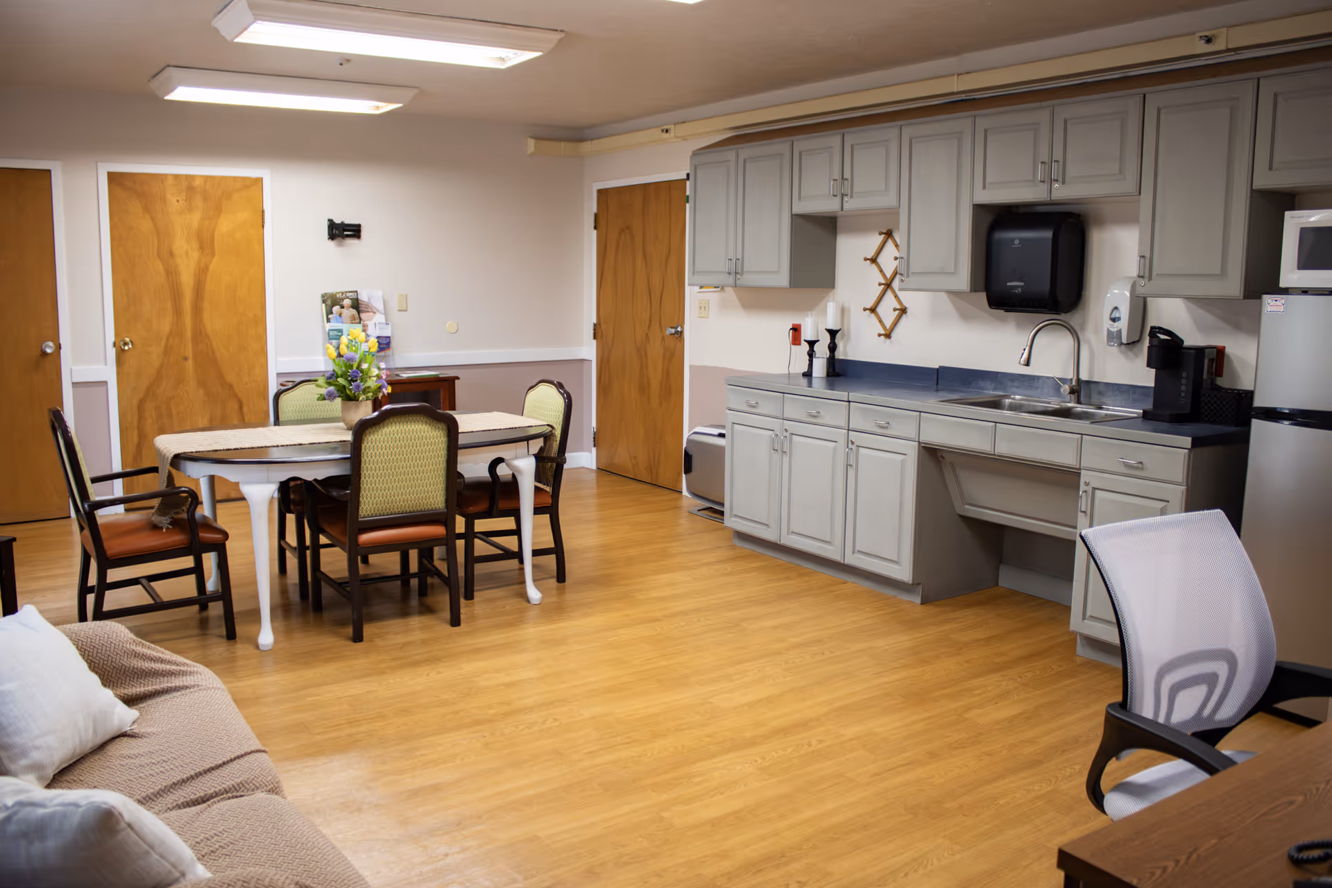 Communal dining area with a table and chairs adjacent to a kitchenette with cabinets and a sink.