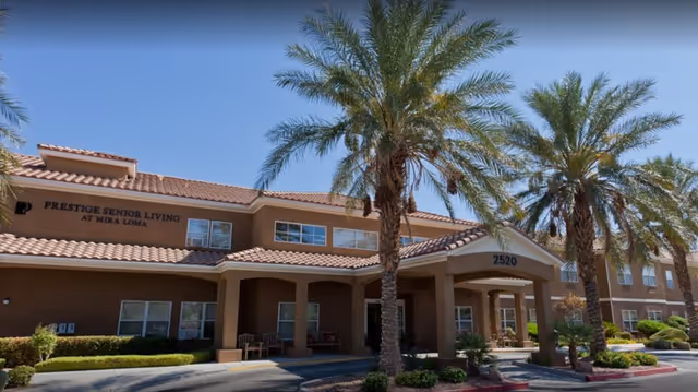 Exterior view of a senior living facility named Prestige Senior Living at Mira Loma, showing a two-story building with a tiled roof, several palm trees in front, and a covered entrance with the number 2520 above it.