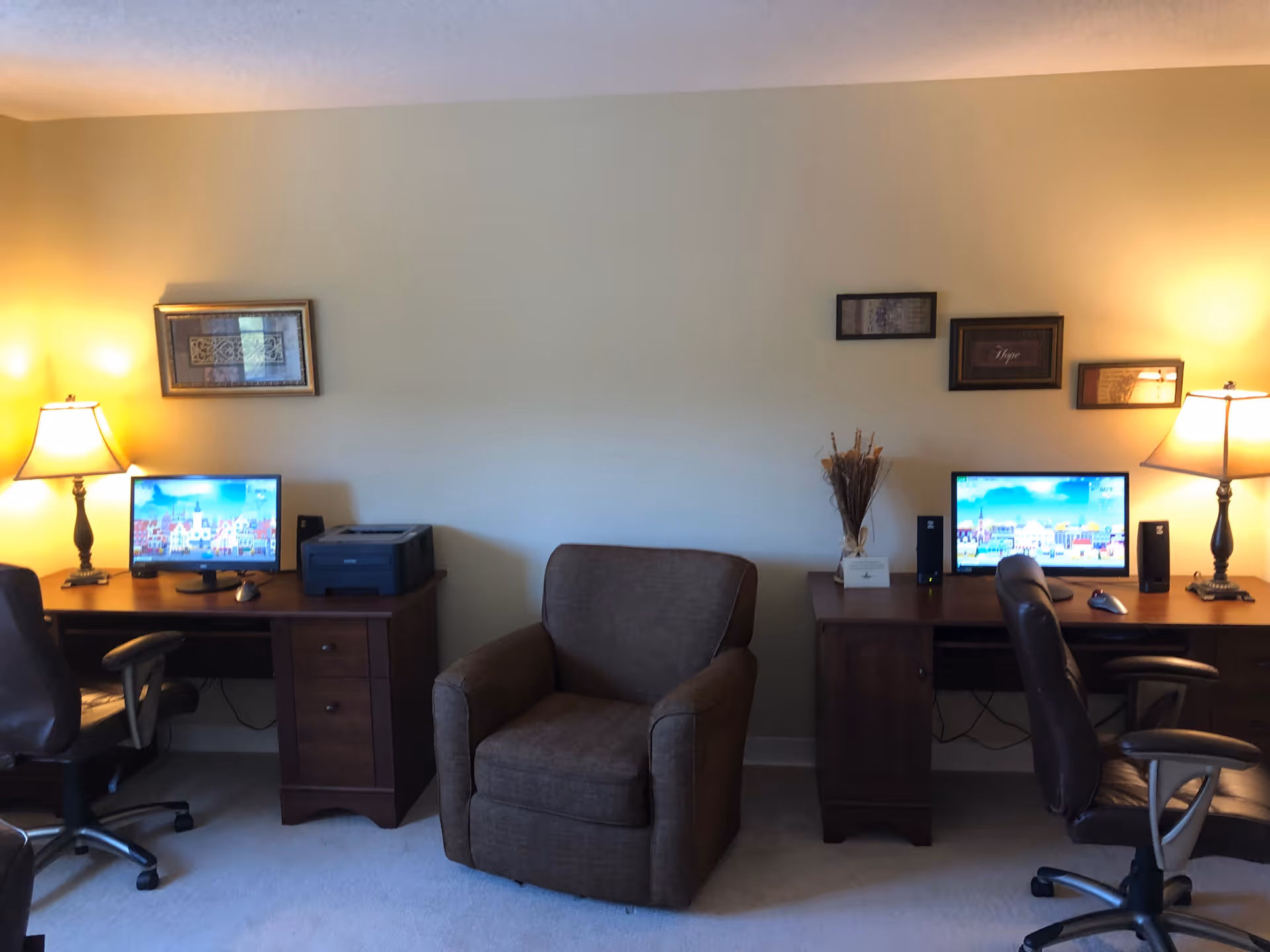Two computer desks with monitors and lamps flank a central upholstered armchair in a cozy common room.