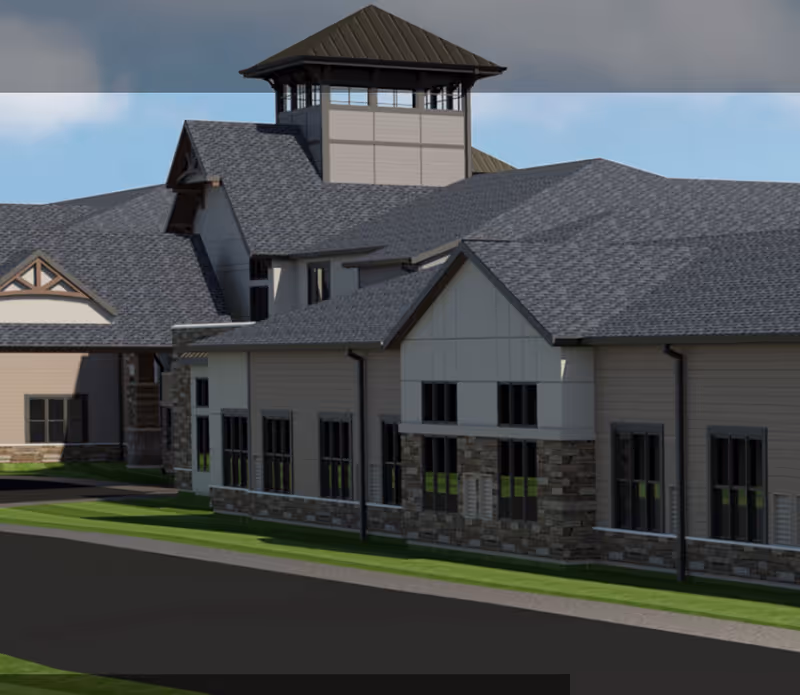 Exterior view of a large building with multiple rooflines, stone and siding facade, and numerous windows, under a clear blue sky.