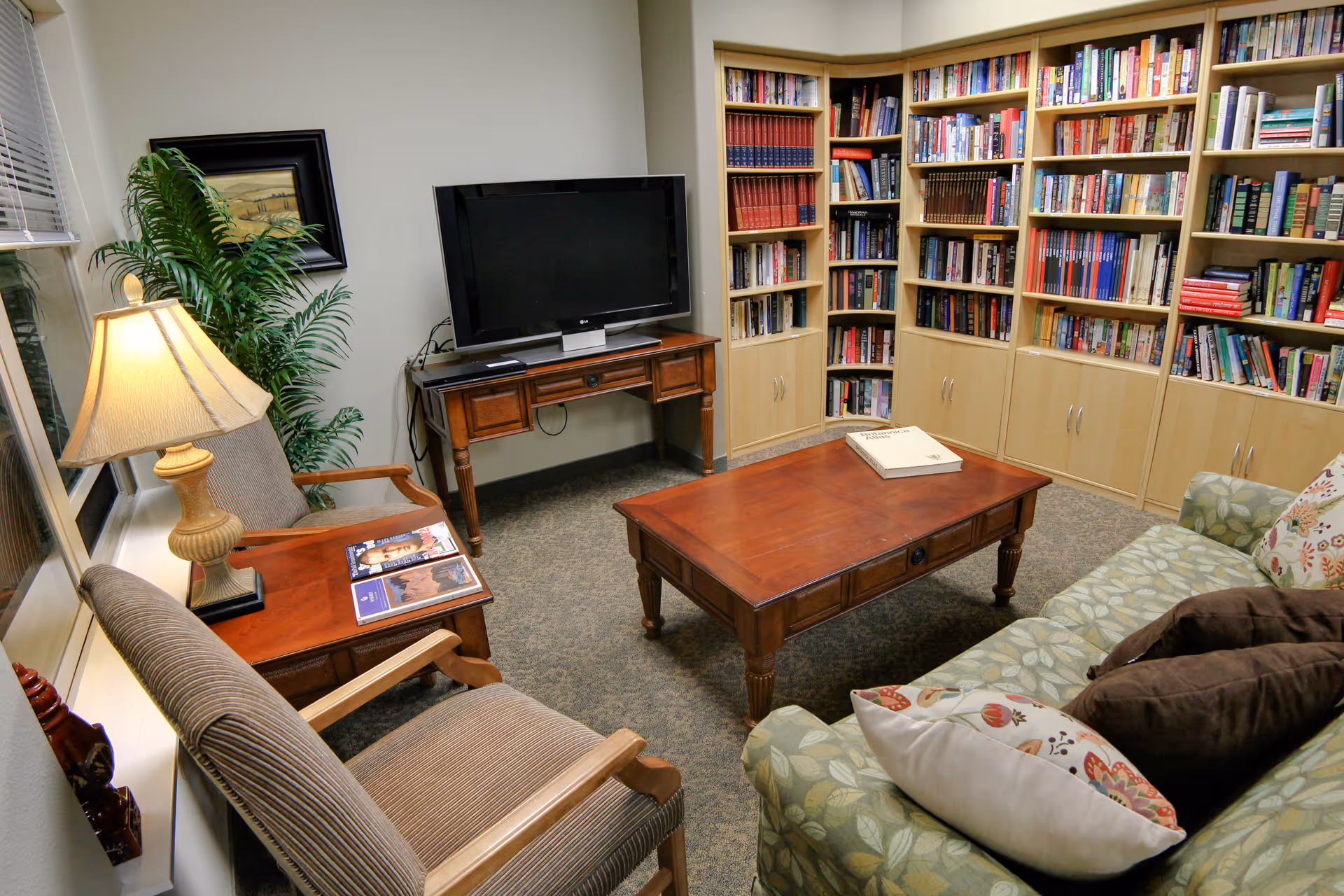 Cozy sitting room with a sofa, armchairs, coffee table, television, and wall-to-wall bookshelves.