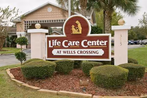 Front view of Life Care Center at Wells Crossing sign with landscaped bushes.