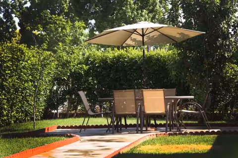 Outdoor patio with table, chairs, and umbrella amid green hedges and lawn.