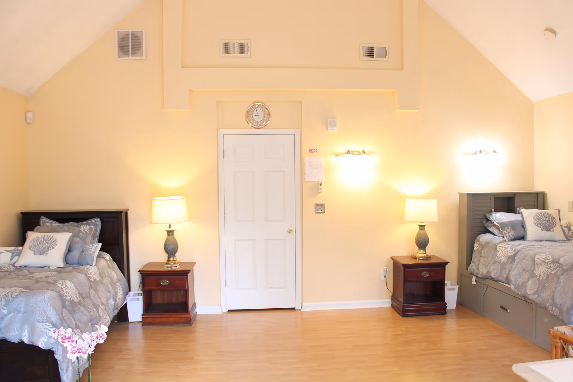 Well-lit bedroom with two twin beds, matching nightstands and lamps on either side of a central door.