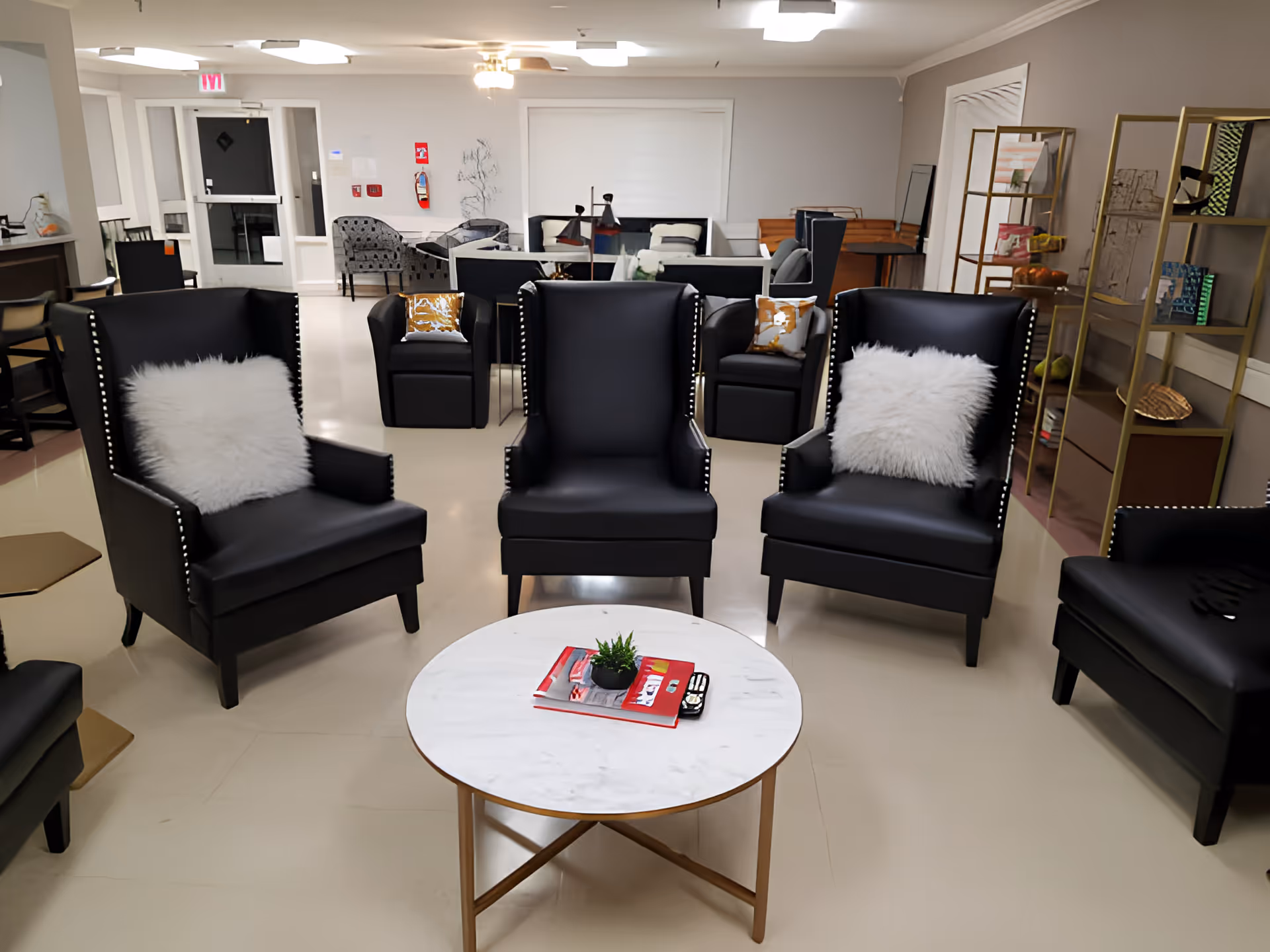 A bright common room with black wingback chairs arranged around a round marble-top coffee table.