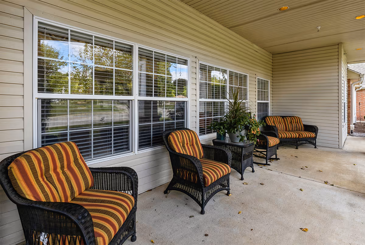 Covered outdoor patio with wicker chairs featuring striped cushions arranged along a building's windows.