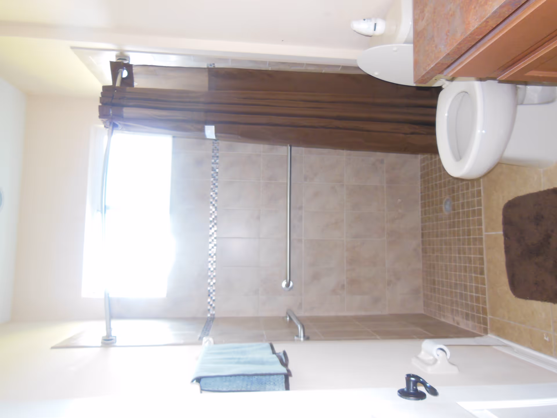 Tiled bathroom with a walk-in shower and brown curtain, grab bar, toilet and sink visible.