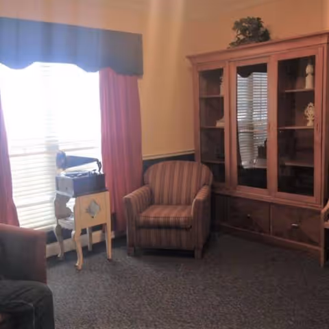Cozy living room with striped armchair, wooden cabinet, and window with red curtains.
