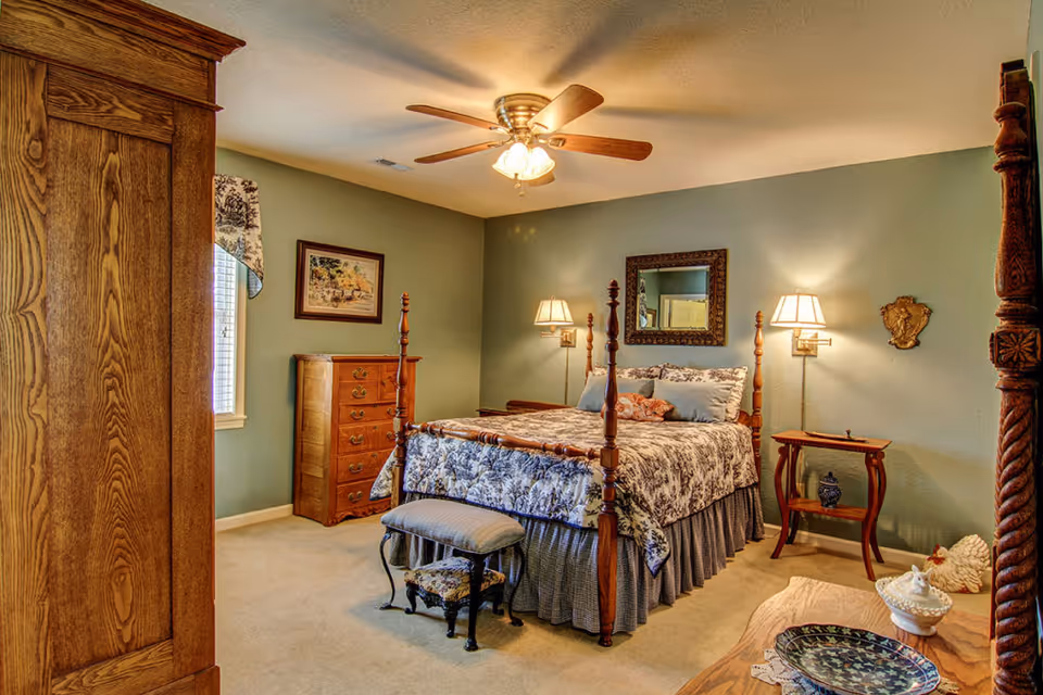 Well-appointed bedroom with a four-poster bed, ceiling fan, wooden furniture, and soft green walls.