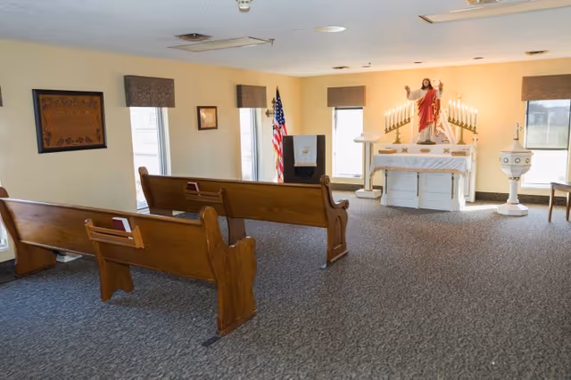 Small chapel-style room with wooden pews facing an altar topped by a statue of Jesus and lit candles.