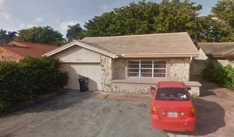Assisted living facility with a stone facade, sloped roof, and a red car in the driveway.