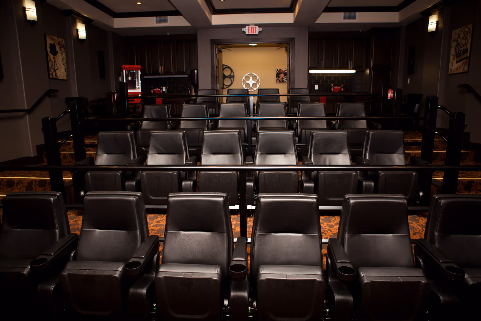 Small private movie theater with rows of black leather reclining seats and a concession area at the back.