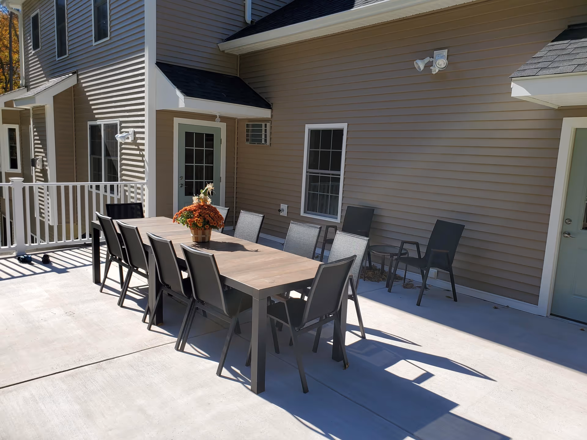 Outdoor patio with a long dining table and chairs next to a beige-sided residential building.