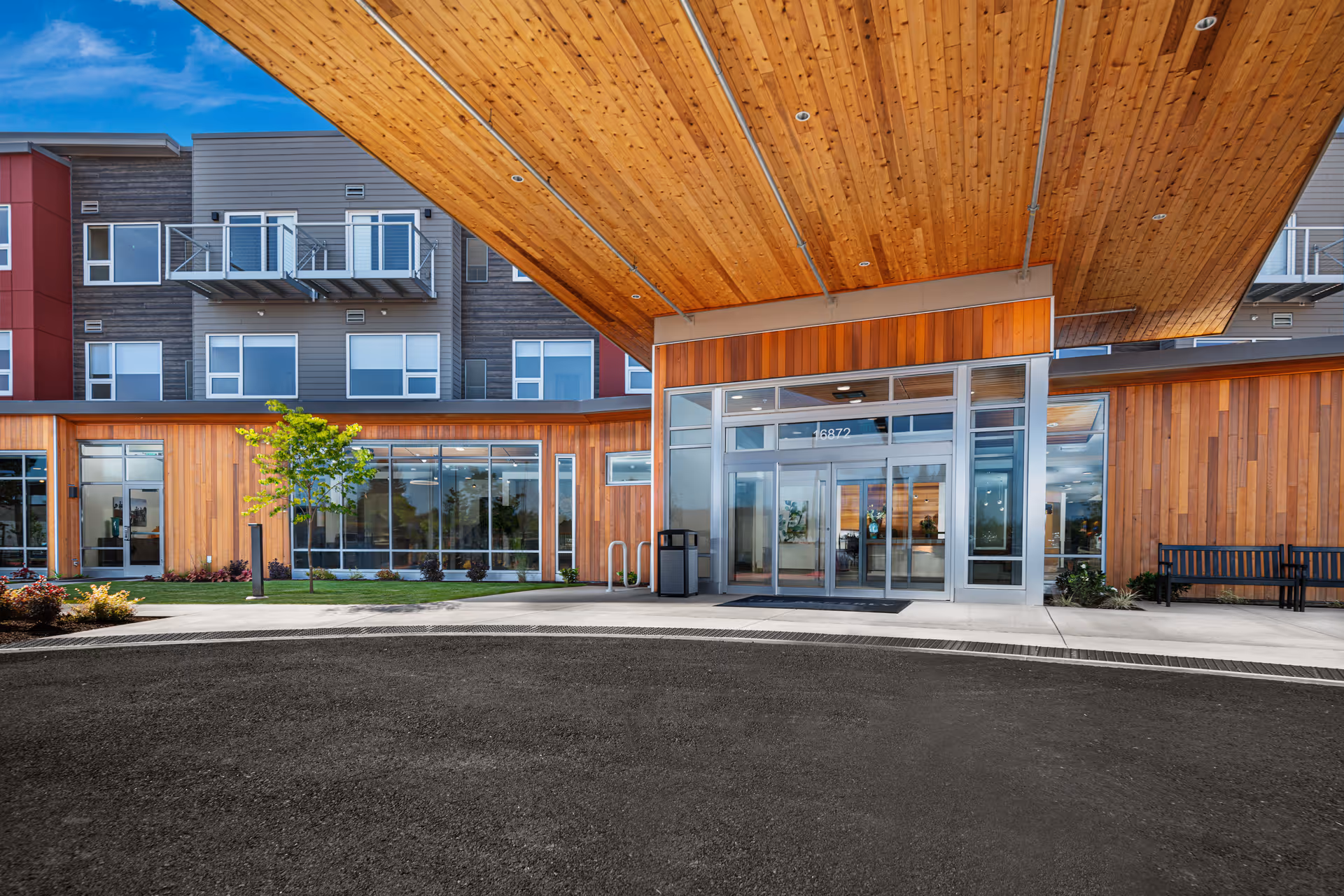 Entrance of a modern senior living building with a large wooden overhang, glass doors, and wood-paneled facade.
