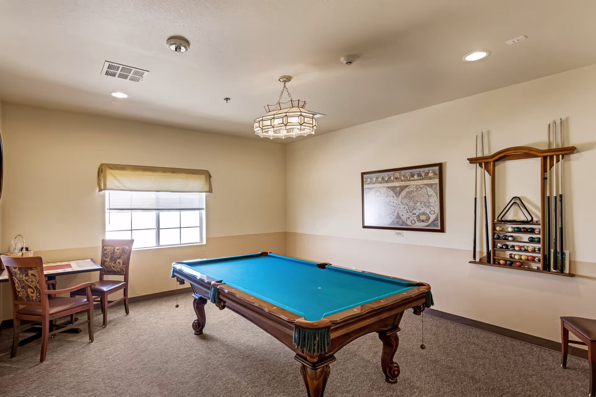 Interior game room with a pool table, cue rack, and a small table and chairs by a window.