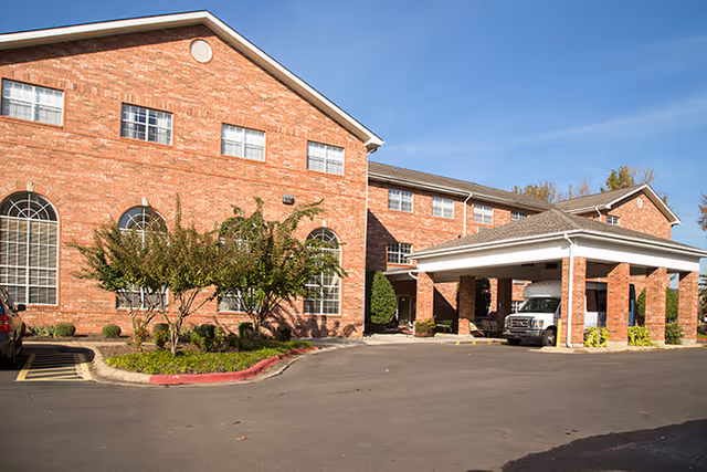 Brick senior living building with arched windows and a covered entrance/porte-cochère with a vehicle parked underneath.