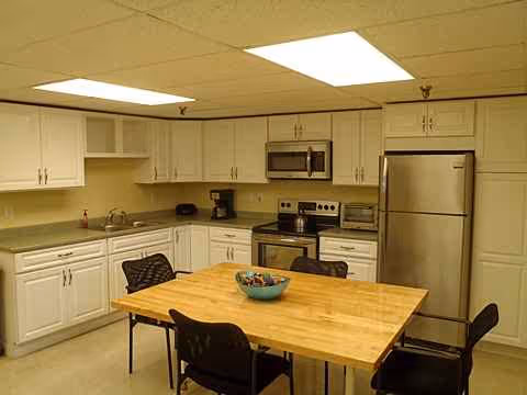 Clean kitchen area with white cabinets, stainless appliances, and a wooden dining table with chairs.