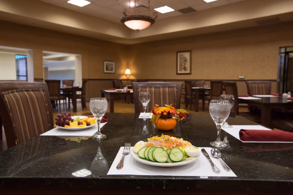 A dining table set with plates of food and glasses of water in a dining area of a senior living facility.
