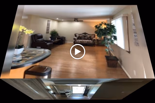 A spacious senior living facility living room with lounge seating, wooden floors, and several potted plants.