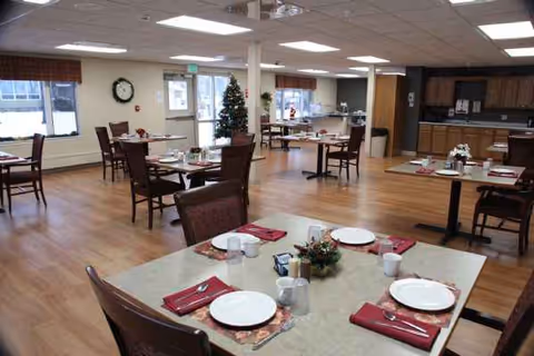 A communal dining room with several tables set and a Christmas tree in the corner.