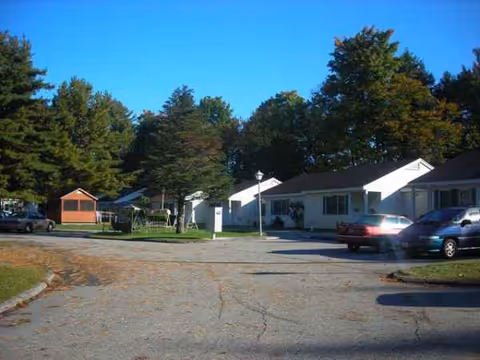 Exterior view of Pinecrest Apartments with parked cars and single-story buildings amid trees.