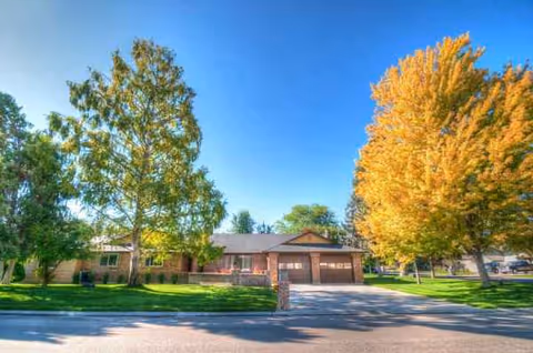 Front view of a single-story brick senior living facility with trees and a driveway.