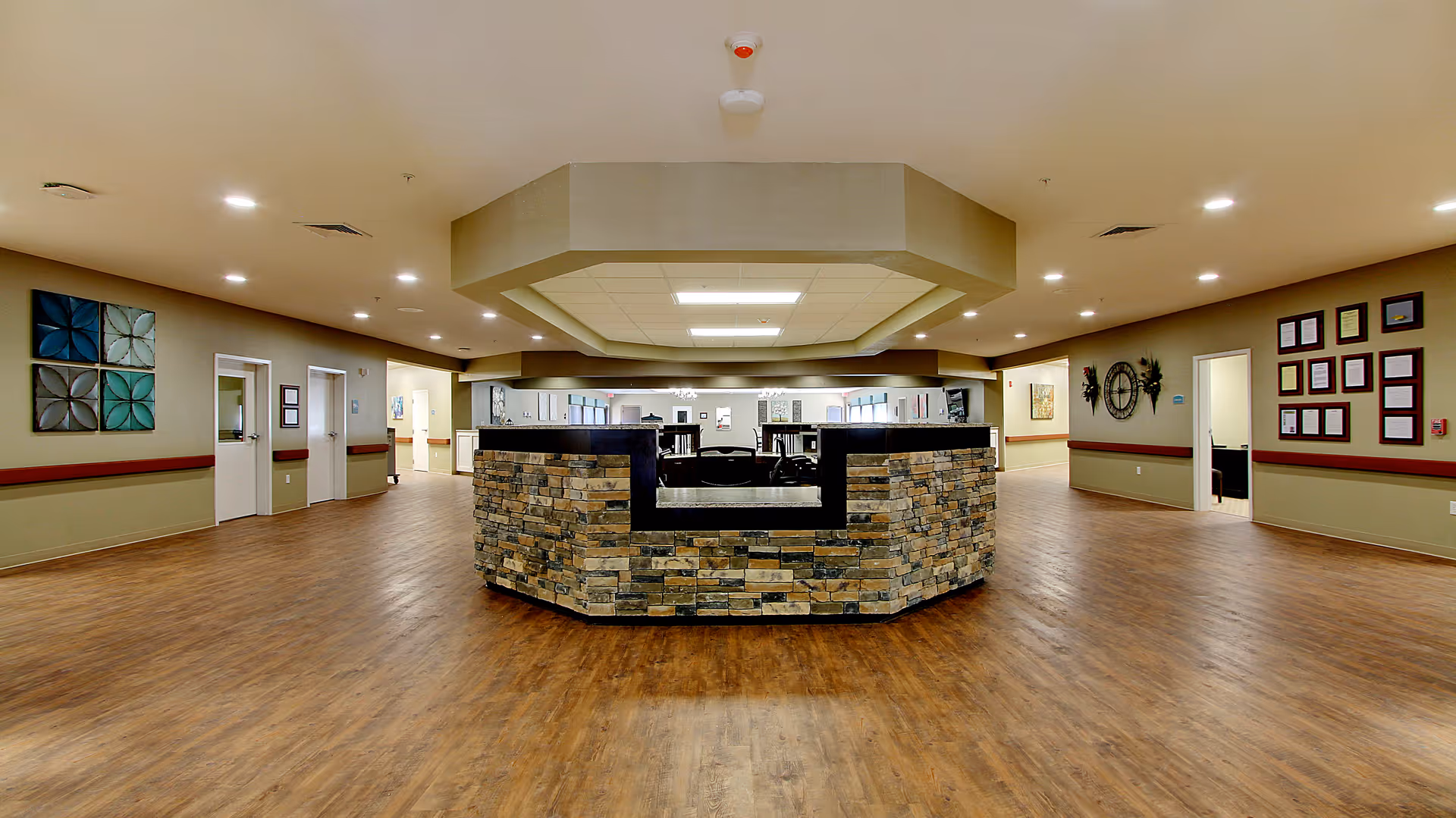 Spacious reception lobby with a central stone-faced desk, wood floors, and hallways leading to rooms.