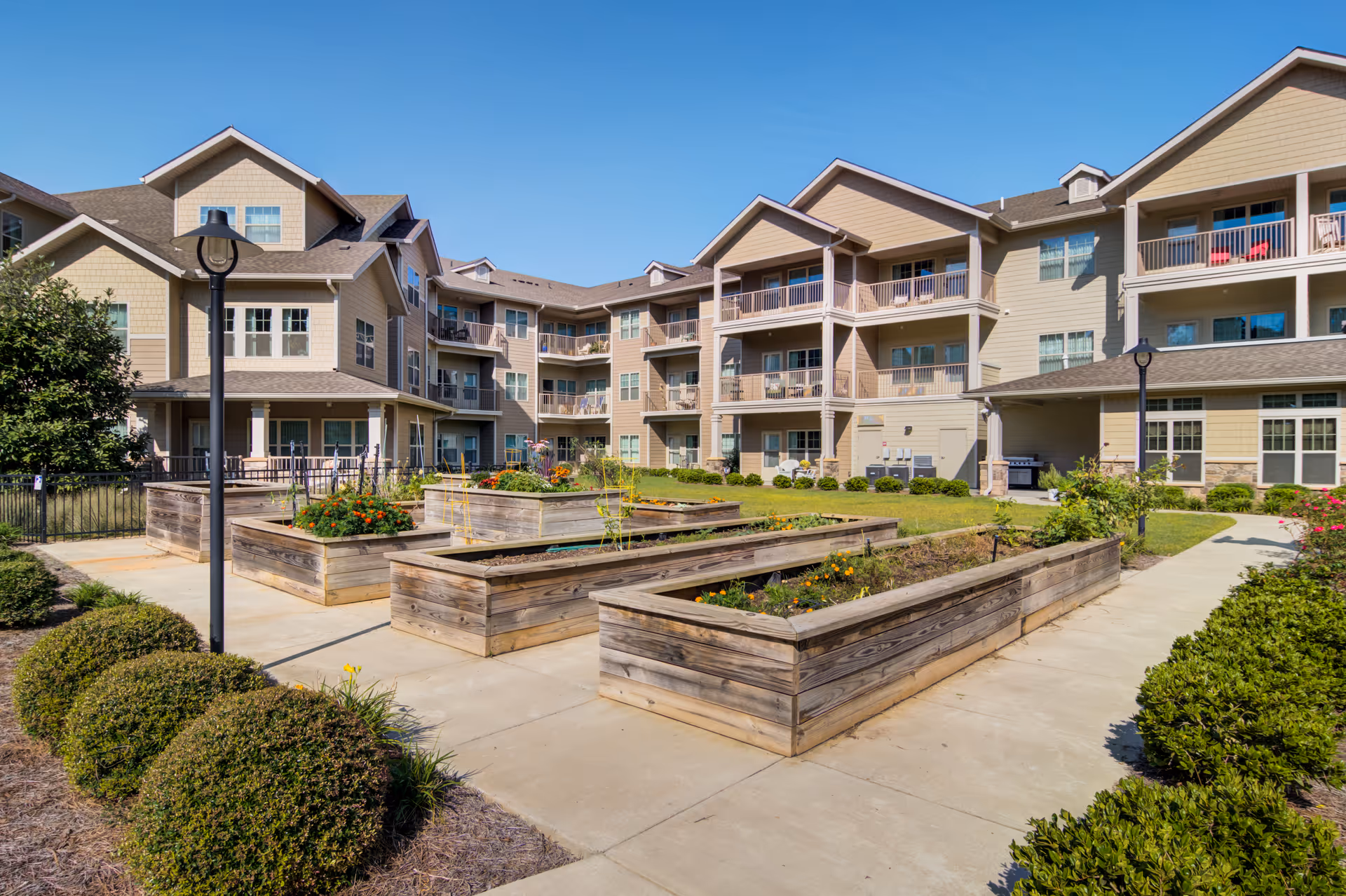 Courtyard of a multi-story senior living building featuring raised wooden garden beds, walkways, and balconies.