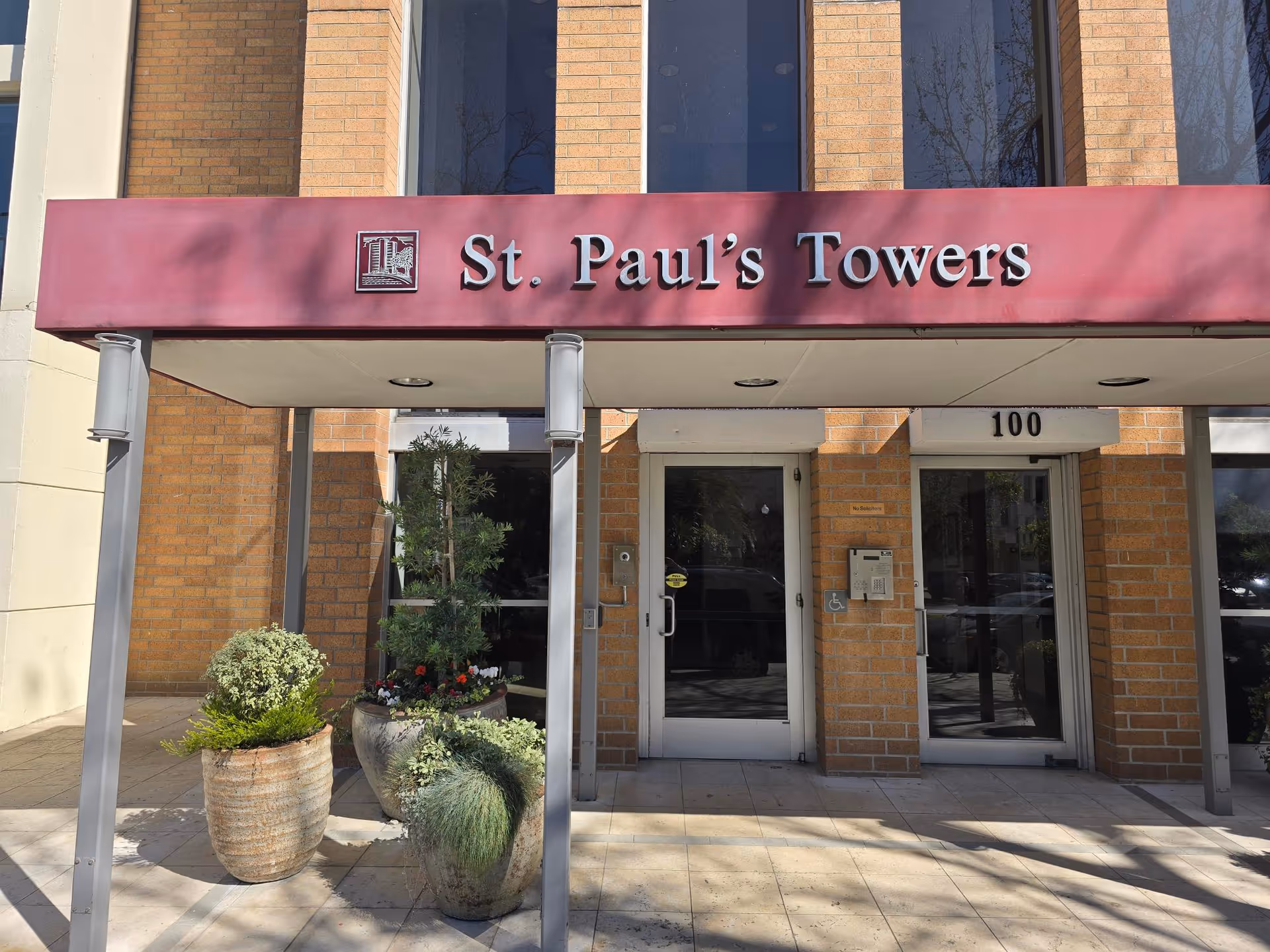 Entrance of St. Paul's Towers with a maroon awning, double glass doors, and potted plants.