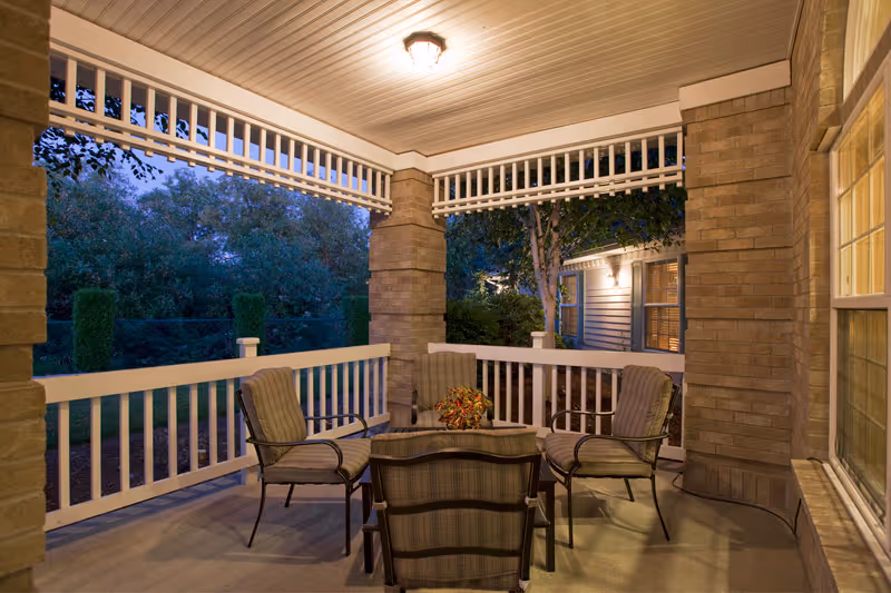 Covered outdoor porch with four cushioned chairs around a small table under a ceiling light.