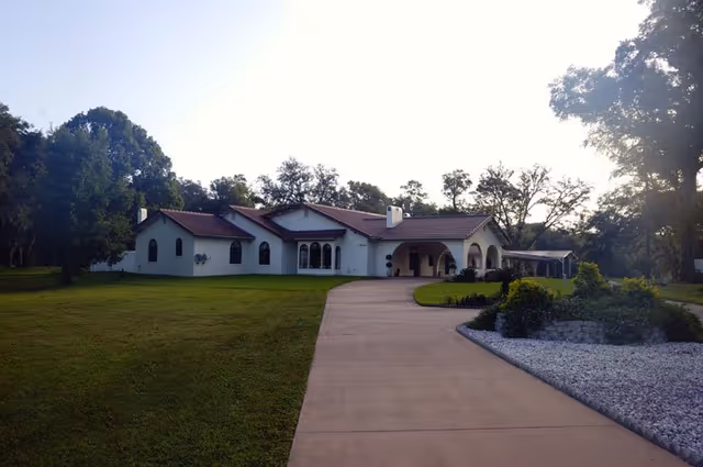 Front exterior of a single-story white building with red-tiled roof and curved driveway.
