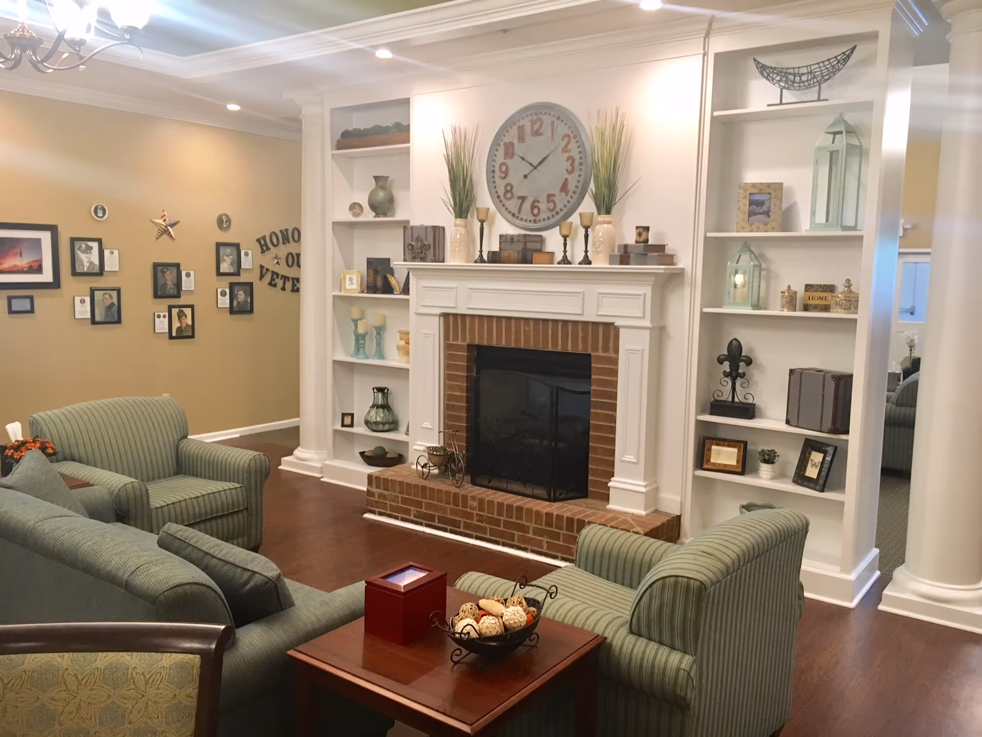 Comfortable communal lounge featuring a brick fireplace with white built-in shelving, green upholstered armchairs, and a coffee table.