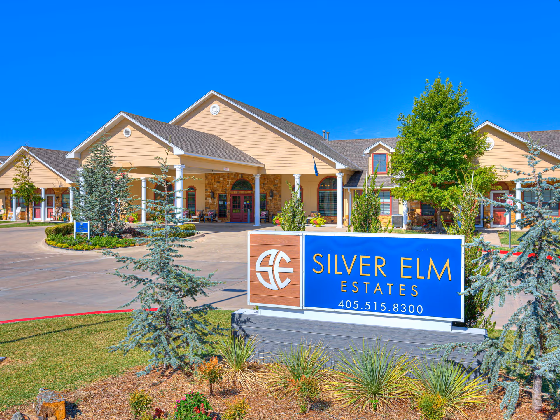 Exterior view of Silver Elm Estates entrance in Norman with blue sign and landscaping.
