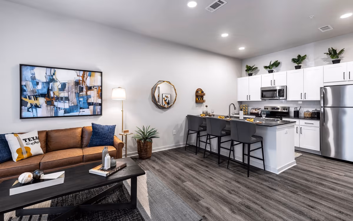 Modern open-plan living room and kitchen with a brown sofa, coffee table, and a breakfast bar with stools.