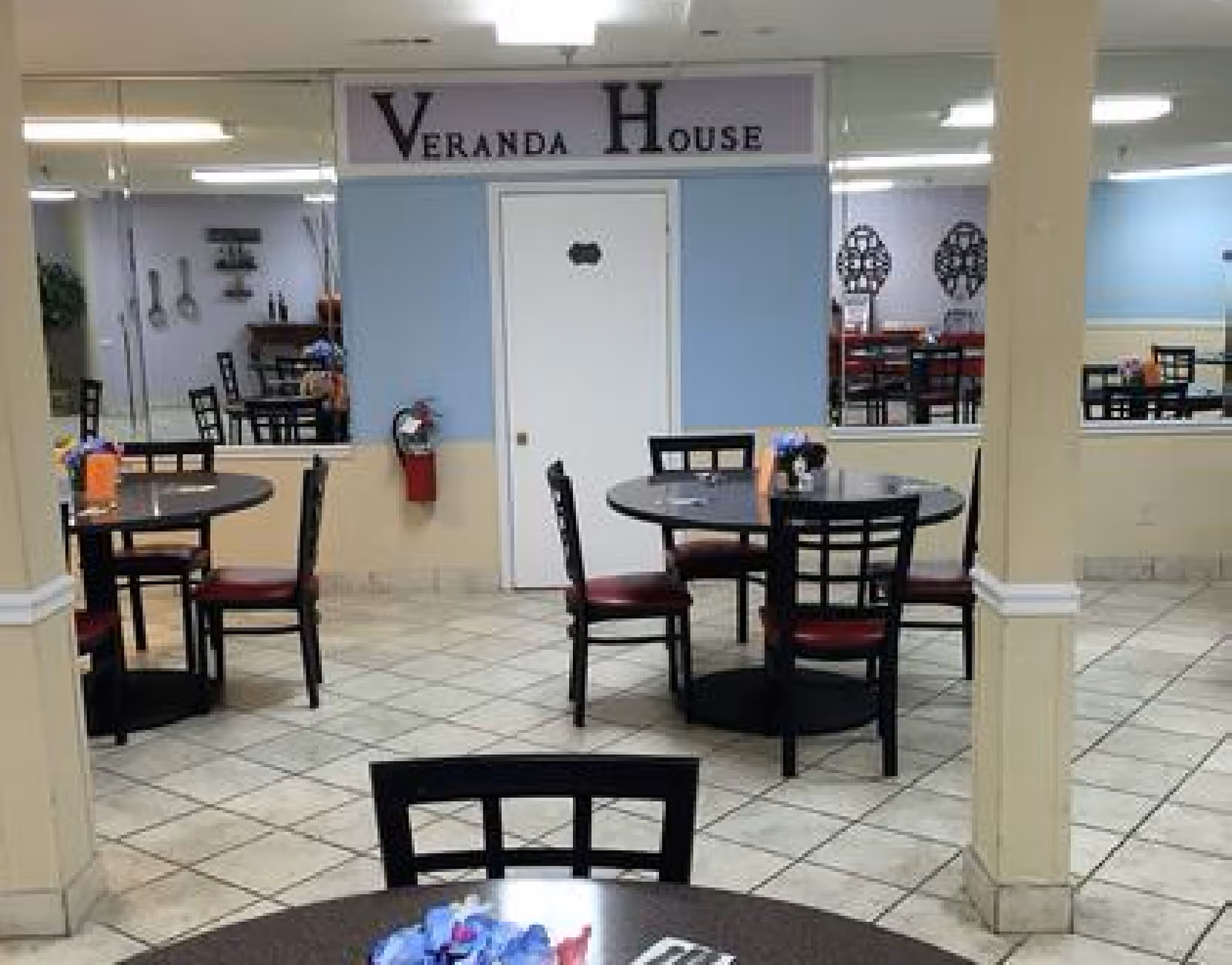 Dining room at Veranda House senior living with round tables and chairs and a sign reading "Veranda House" above a doorway.