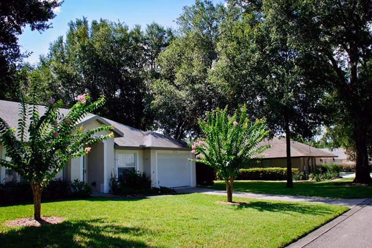 Single-story homes with garages, green lawns, and trees along a sunny residential street.