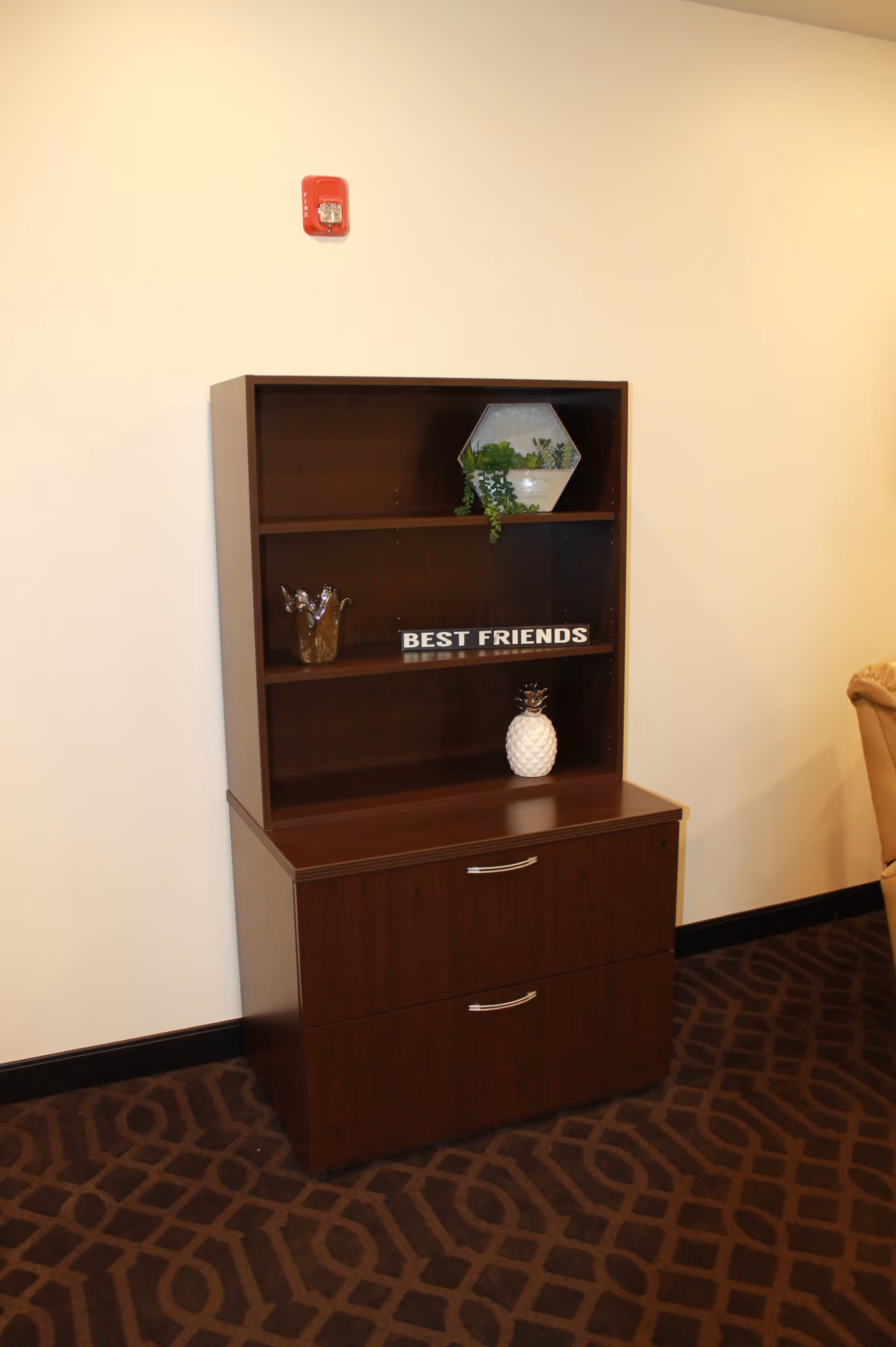 Dark wood shelving unit with decorative items including a "BEST FRIENDS" sign and a faux pineapple against a beige wall.