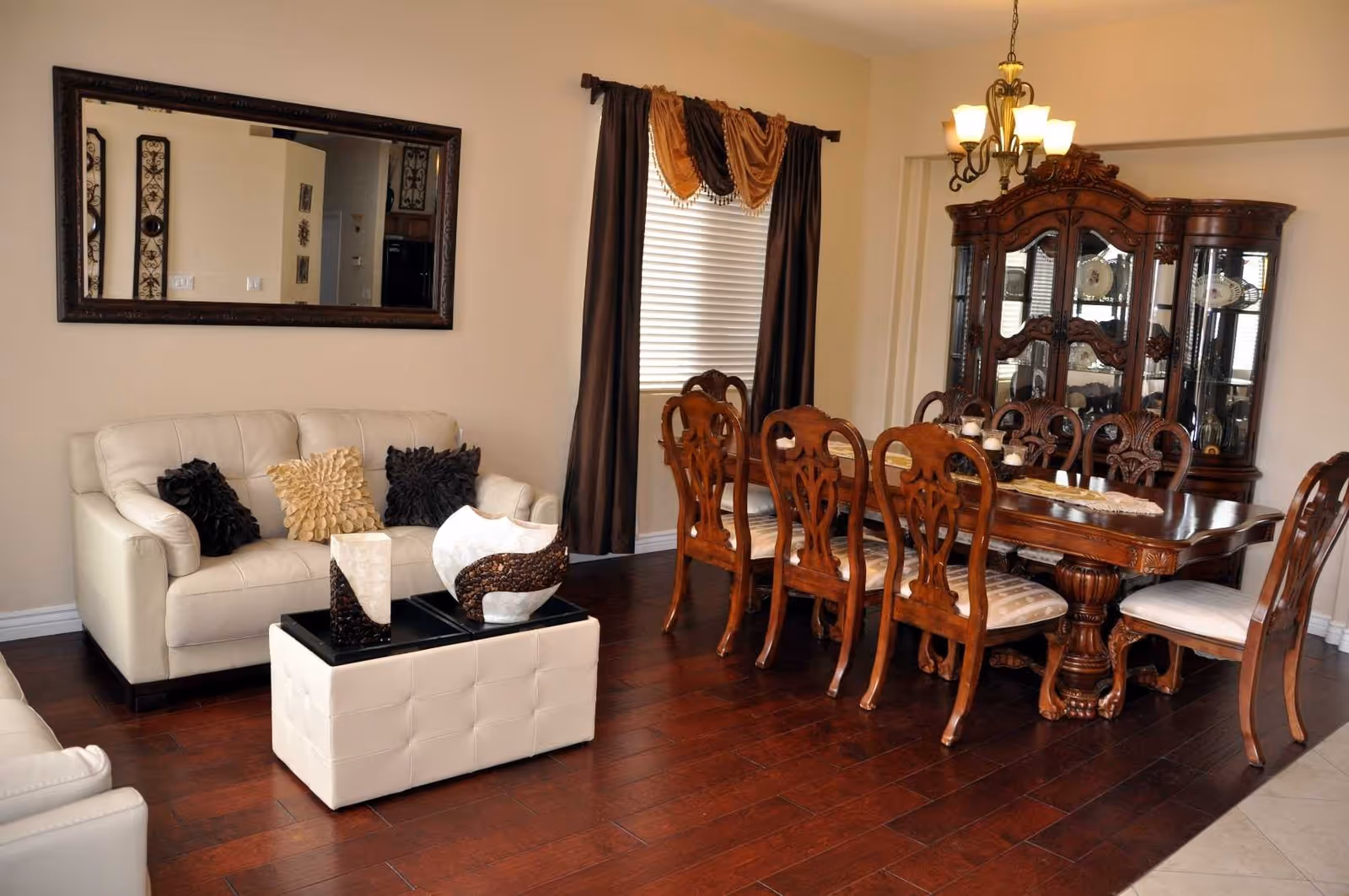 A combined living and dining room with a white leather sofa, a wooden dining table and chairs, a china cabinet, decorative accents, and hardwood floors.