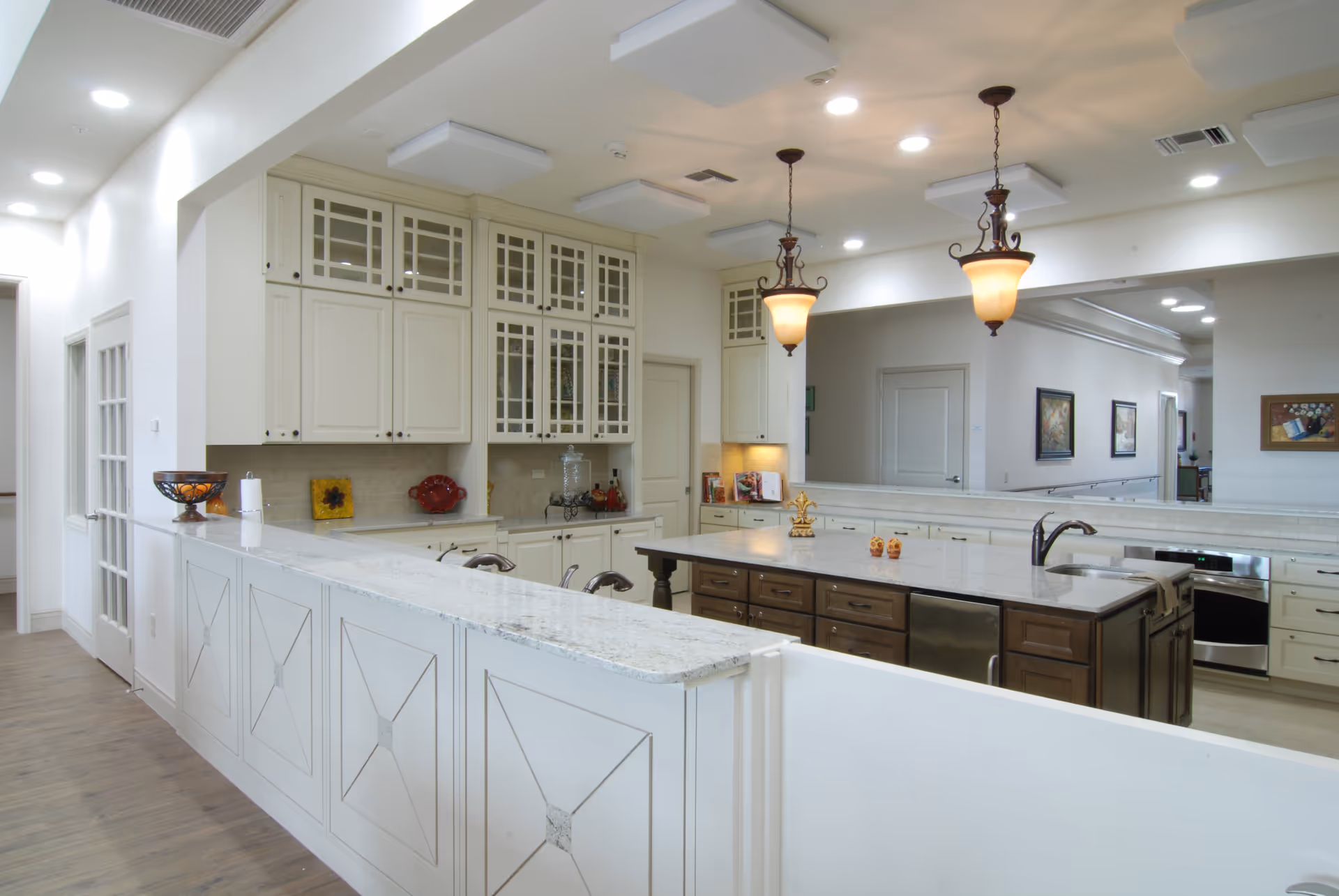 Bright communal kitchen with a large center island, white cabinets, pendant lights, and granite countertops.