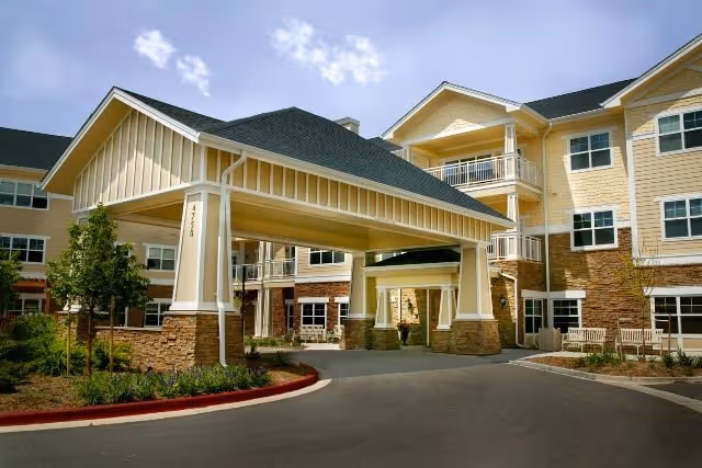 Exterior view of MacKenzie Place, a beige multi-story senior living building with a covered entrance.