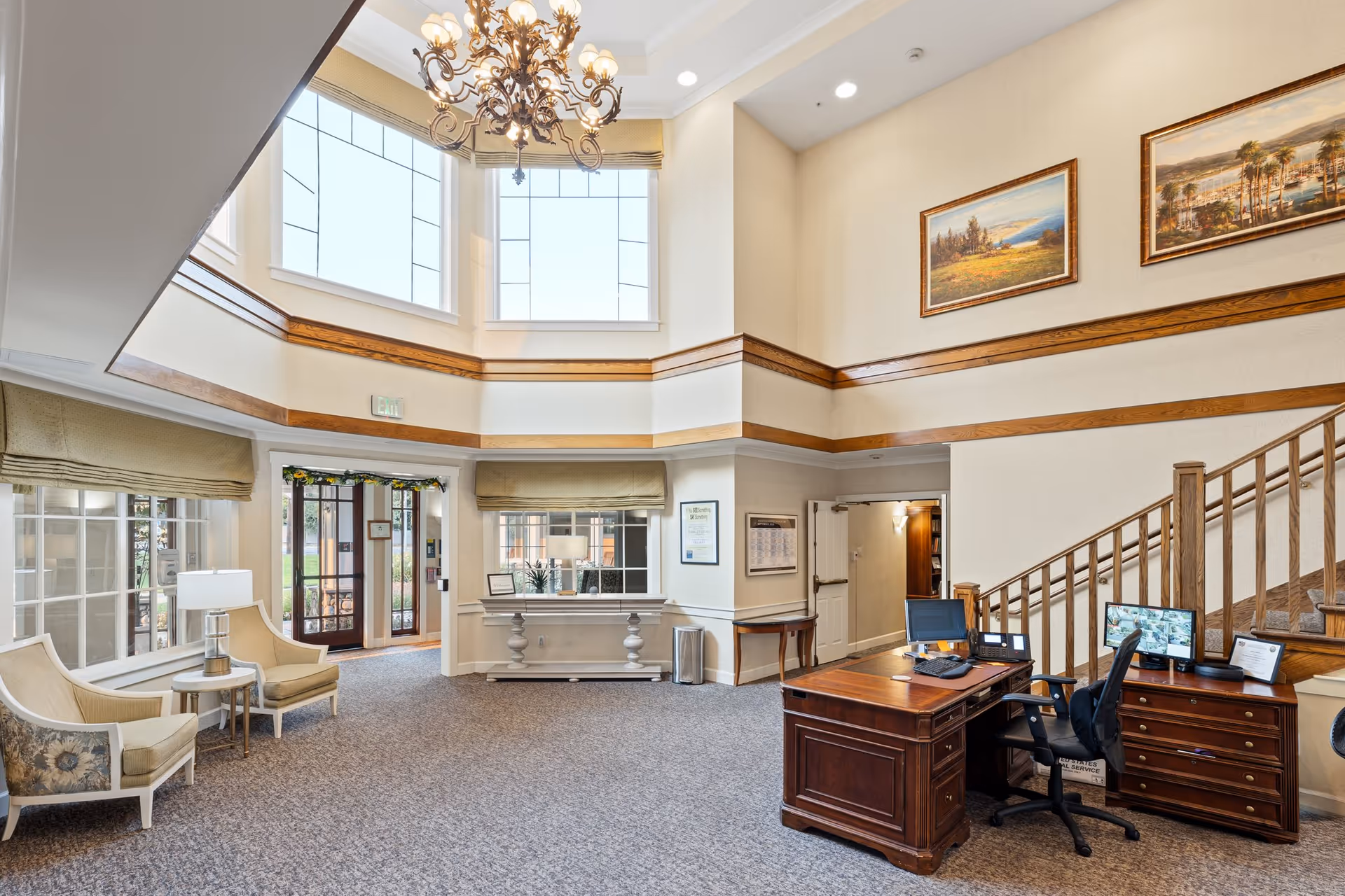 Bright two-story lobby with seating area, reception desk, chandelier, staircase and large windows.